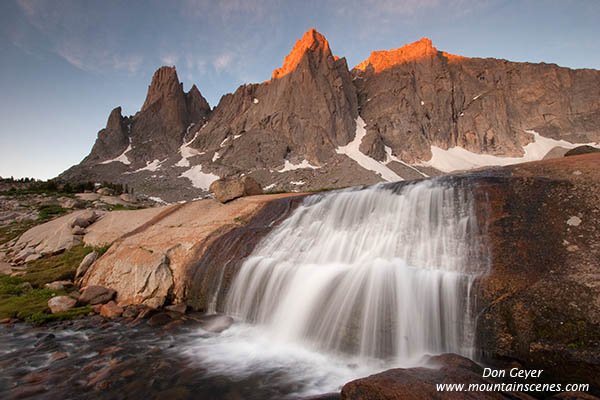 Picture of alpenglow on Warrior and Warbonnet Peaks above a waterfall.